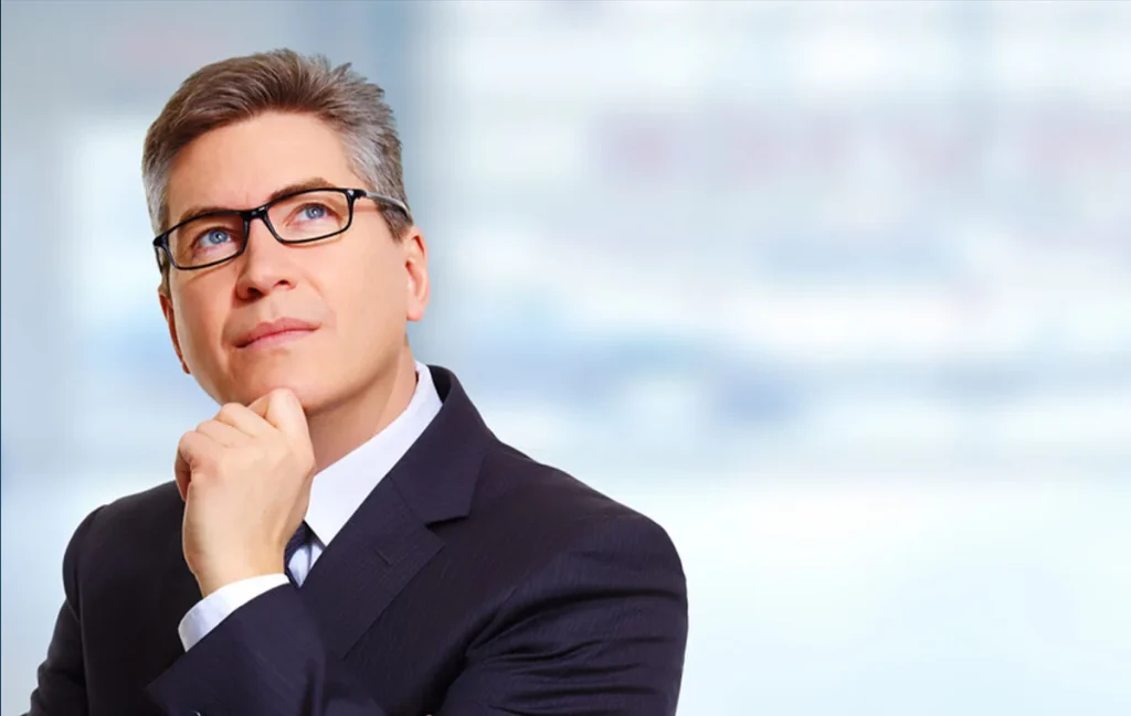 Thoughtful businessman in a suit reflecting on strategic growth and challenges of scaling a business against a blurred office background.