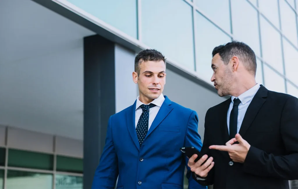Two business executives reviewing mobile data while discussing offshore development companies collaboration strategy.